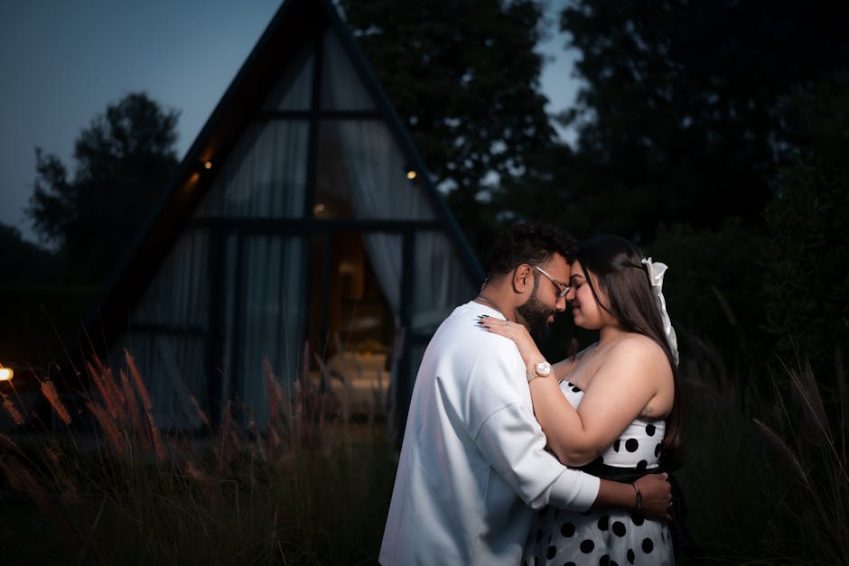 Couple embraces near a modern cabin at dusk.