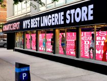 Romantic Depot storefront with bold sign 'NY’s Best Lingerie Store' and mannequins in colorful lingerie displayed in the window