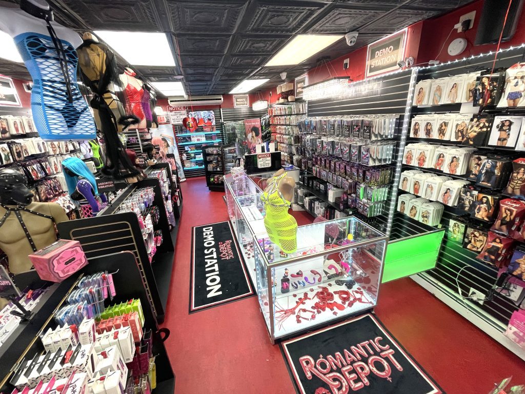 Romantic Depot store interior with lingerie displays, sex toys, and adult gifts on red carpeted showroom floor