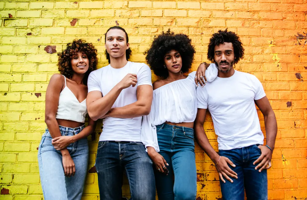 Group of stylish young Black adults posing against a colorful yellow and orange brick wall, celebrating culture, freedom, and self-expression during Juneteenth and Pride.