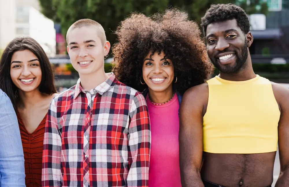 Diverse LGBTQ+ friends smiling together outdoors, celebrating Pride and self-expression in inclusive community spirit.