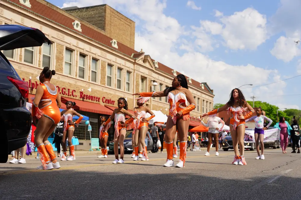 Black youth dance team performing in vibrant orange outfits during a Juneteenth street celebration in front of NYC community center.