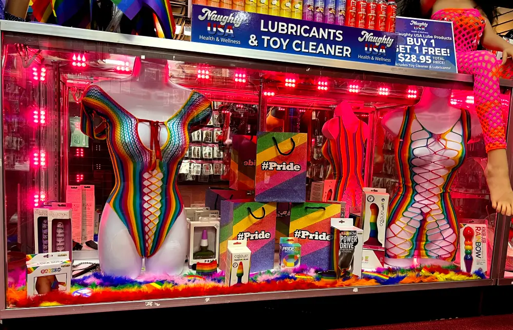 Pride display at Romantic Depot featuring rainbow lingerie, sex toys, lubricants, toy cleaners, and glittery #Pride gift bags under pink lighting