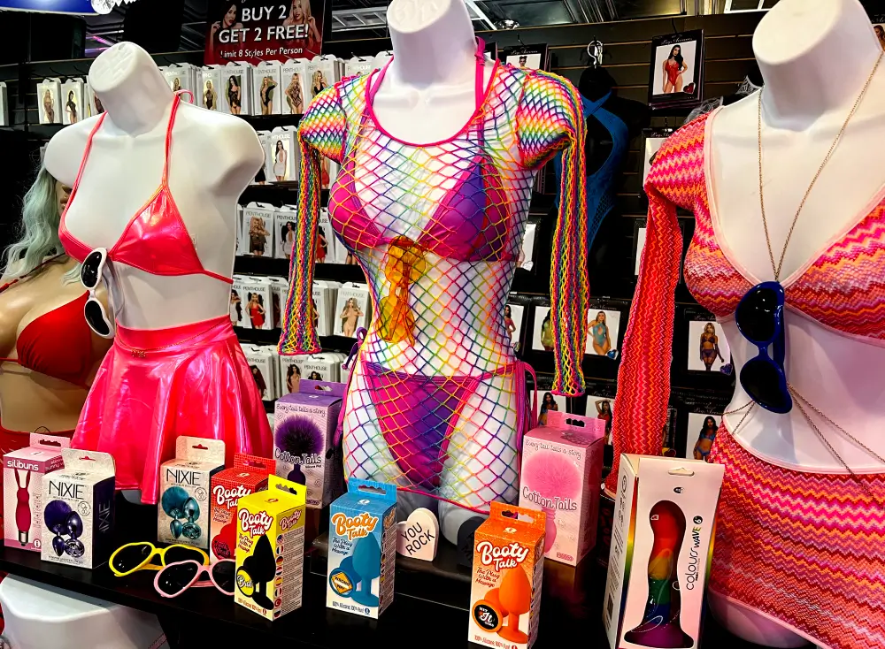 Pride-themed mannequins in rainbow and pink lingerie with Booty Tails plugs, rainbow vibrator, and novelty items at Romantic Depot display