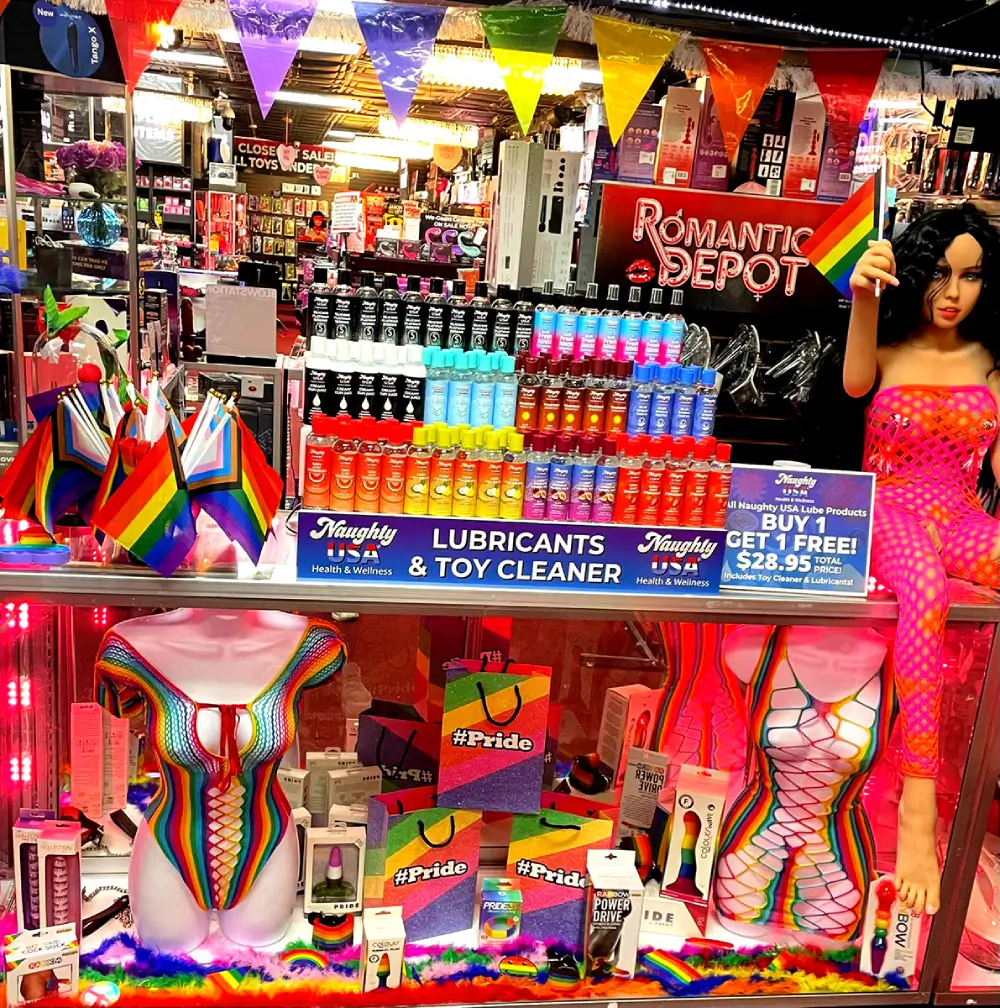 Romantic Depot Pride display with rainbow flags, lubricants, lingerie, and adult toys under colorful banners and pink lighting