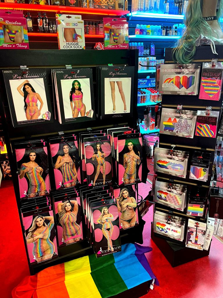 Rainbow-themed lingerie and accessories display at Romantic Depot, featuring Pride bodystockings, men’s thongs, nipple pasties, and inclusive apparel.