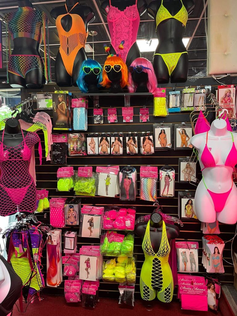 Bright neon lingerie and rave wear display at Romantic Depot, featuring fishnet bodysuits, wigs, and colorful accessories perfect for Pride and self-expression.