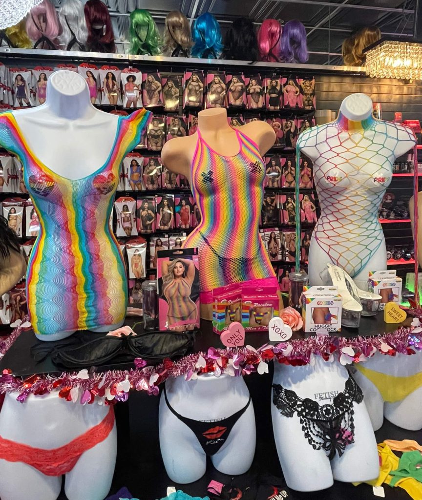 Colorful Pride-themed lingerie display at Romantic Depot featuring rainbow fishnet bodysuits, thongs, and novelty apparel, celebrating LGBTQ+ inclusivity and expression.