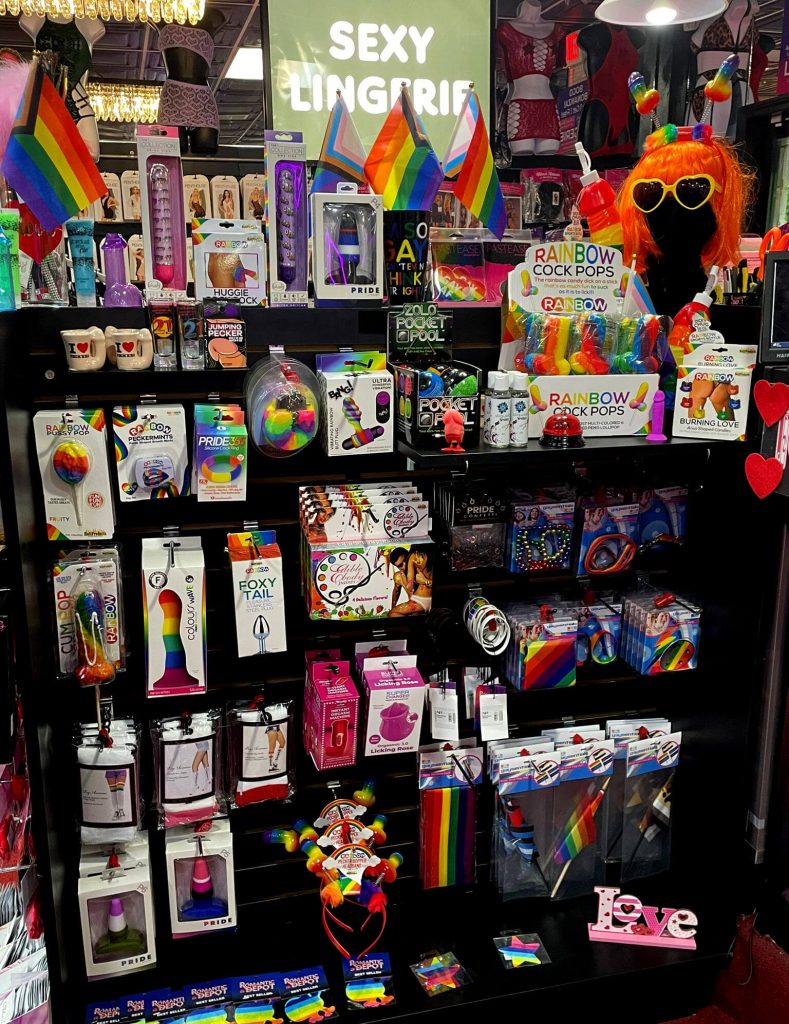 Romantic Depot Pride display shelf featuring rainbow flags, colorful sex toys, novelty items, and LGBTQ+ accessories celebrating love, freedom, and inclusivity.