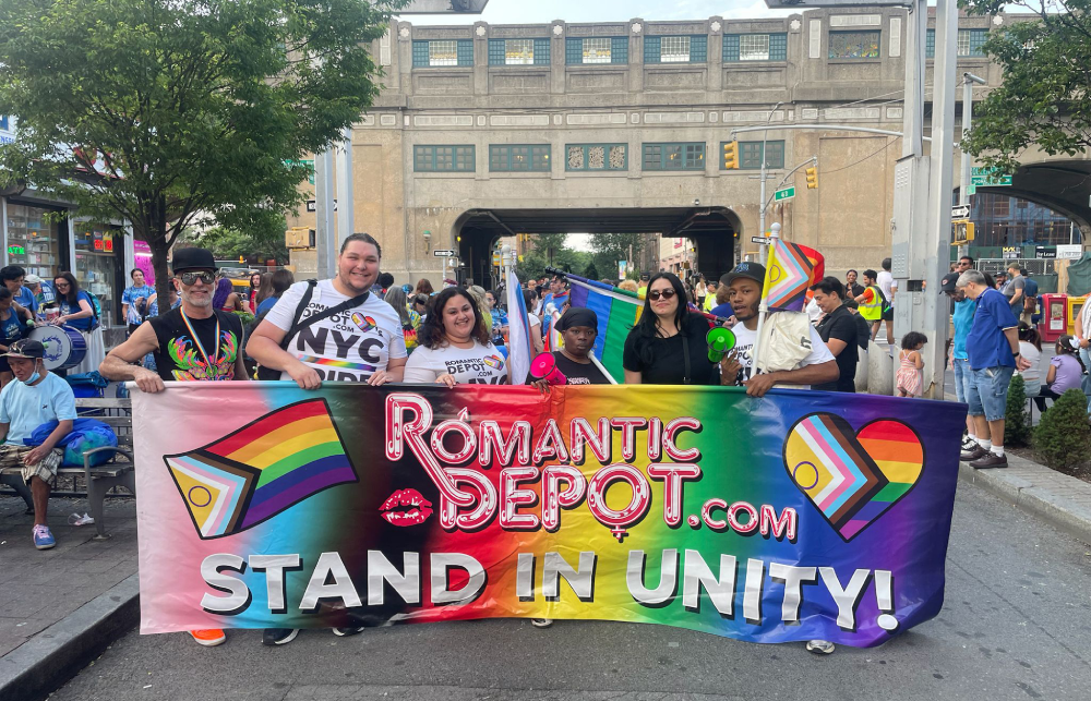 Romantic Depot staff and supporters holding a Pride banner that reads 'Stand in Unity!' at SunnyPride LGBTQ+ parade in NYC.