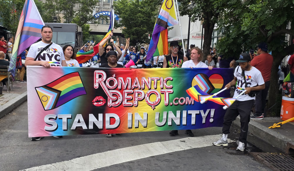 Romantic Depot staff holding a rainbow banner that reads 'Stand in Unity' at SunnyPride, celebrating LGBTQ+ pride and inclusion in New York City.