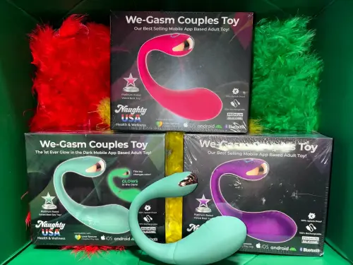 We-Gasm Couples Toy – glow-in-the-dark, app-controlled vibrating sex toy for couples, shown in rainbow Pride display. Compatible with iOS & Android.